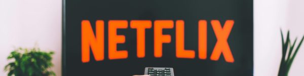 A hand holding a TV remote in front of a screen with Netflix, perfect for streaming and movie night themes.